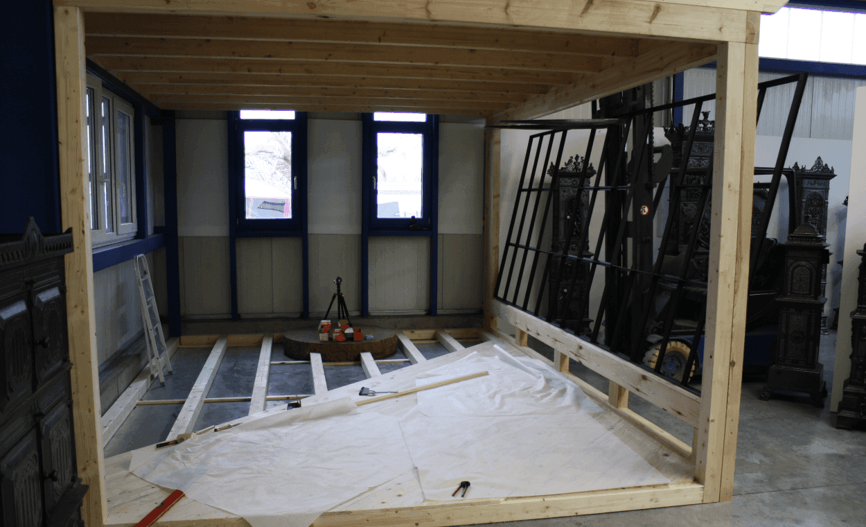 Zu sehen ist der Aufbau eines in der Halle befindlichen Besprechungsraums. Zentral ist ein großer Mühlstein, der im Hallenboden eingelassen ist. Die Wände bestehen zu großen Teilen aus alten Fabrikfenstern.